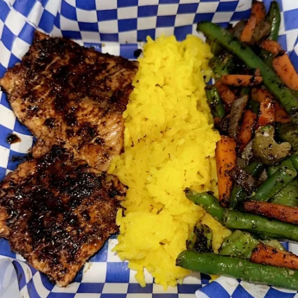 Smokey Sensations' BBQ salmon with yellow rice and roasted green beans and carrots in a checkered basket.