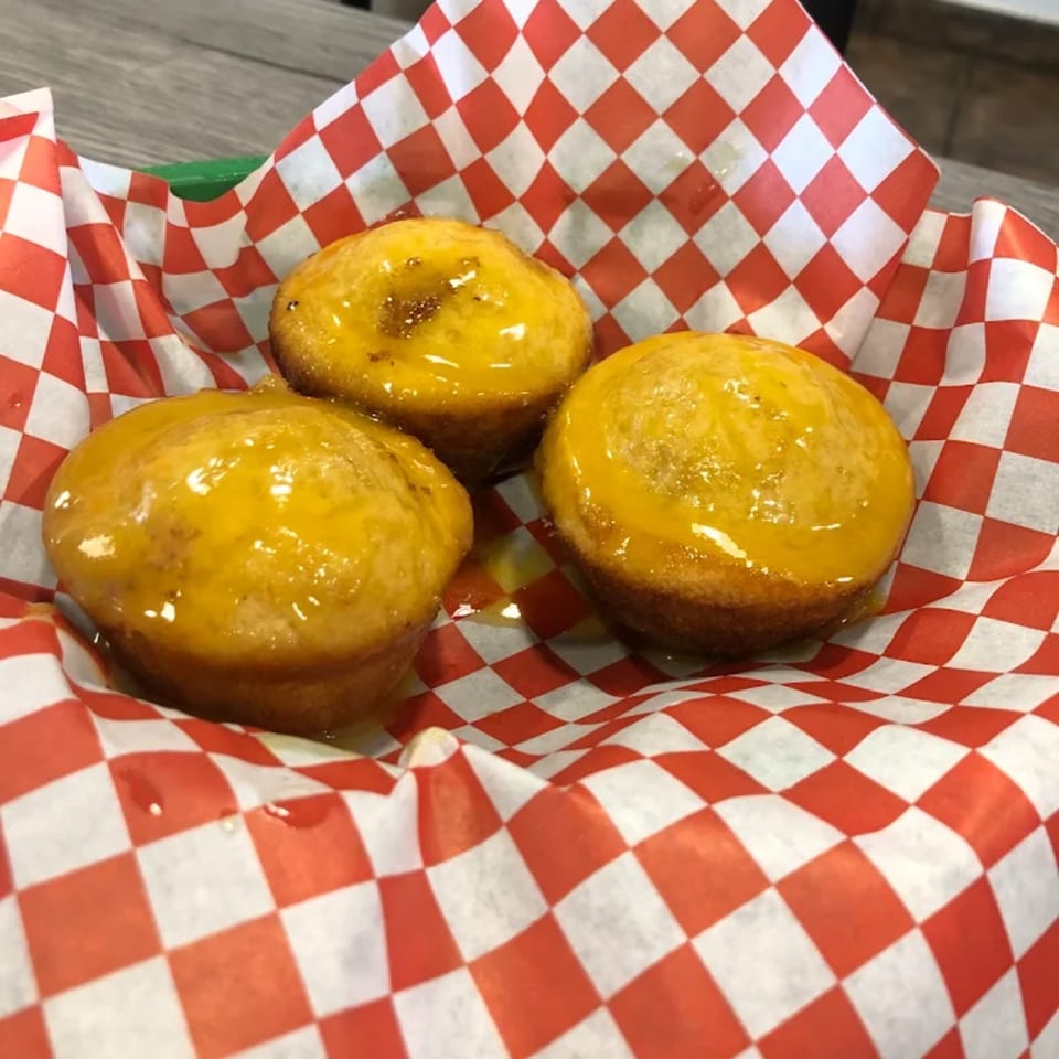 Three golden-brown hush puppies, glistening with a sweet glaze, served in a red and white checkered paper.