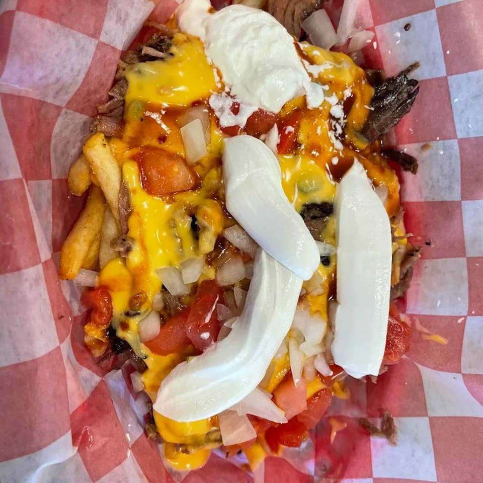 Smokey Sensations' loaded fries with melted cheese, chopped tomatoes, onions, and sour cream in a red checkered basket.