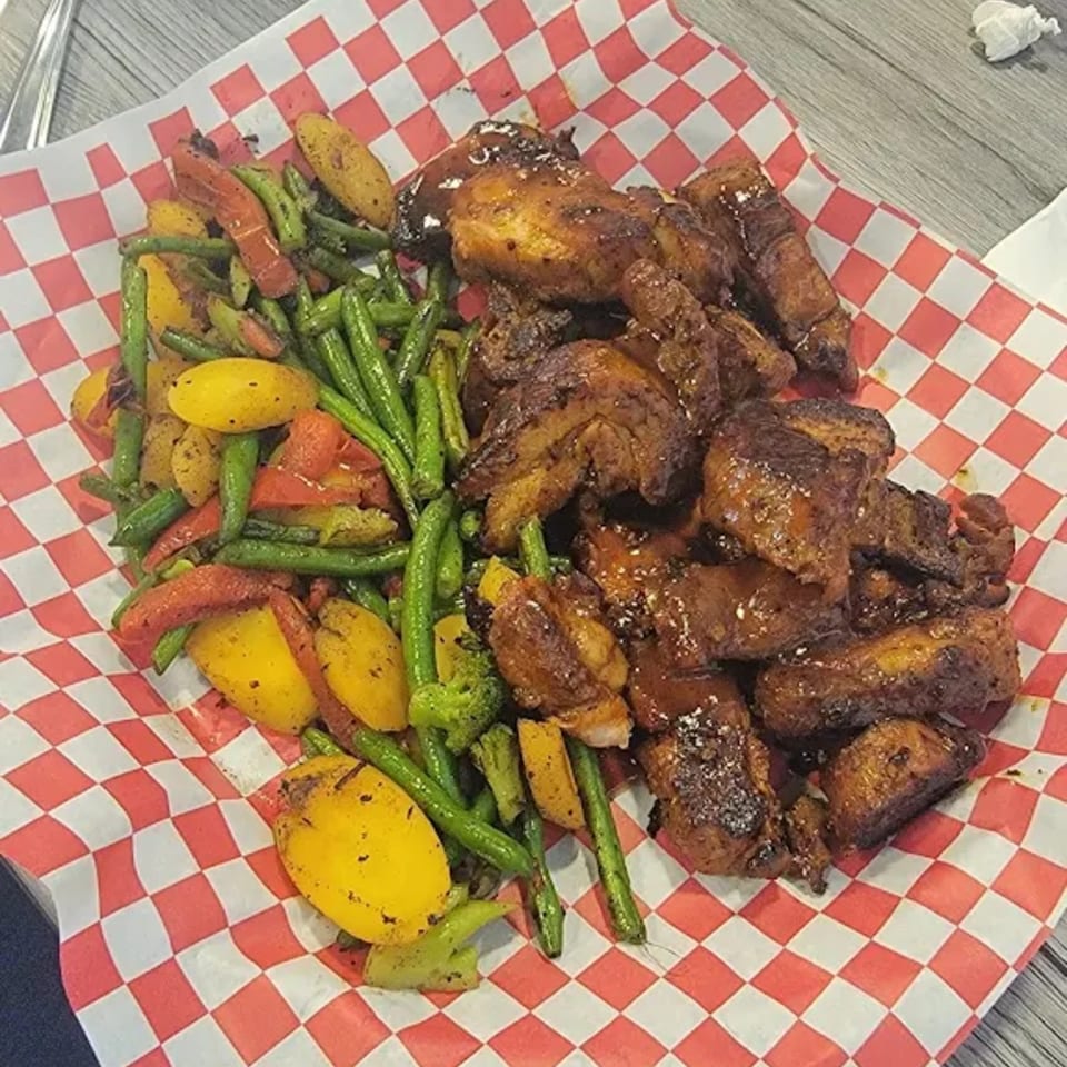 Smokey Sensations' BBQ chicken wings and roasted vegetables served on red and white checkered paper.