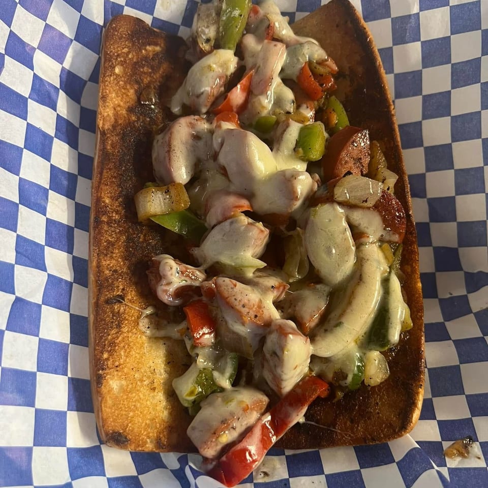 Smokey Sensations' cheesy sausage and pepper sandwich on a toasted bun, served on checkered paper.